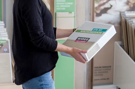 wineo Musterbox Frau mit schwarzem Oberteil hält kostenlose wineo Fußboden Musterbox in der Hand