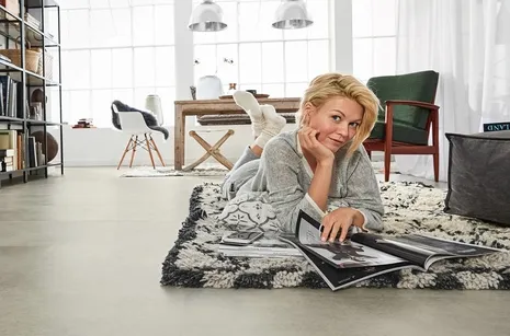 Designboden wineo 600 Frau liegt auf einem Teppich im Esszimmer mit grauem Vinylboden in Betonoptik